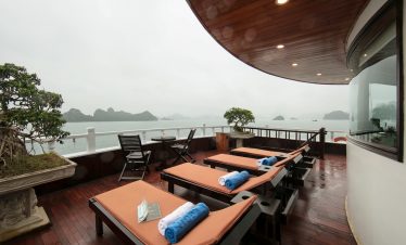 Scenic view of Halong Bay from a luxury cruise balcony with lounge chairs and relaxing atmosphere.