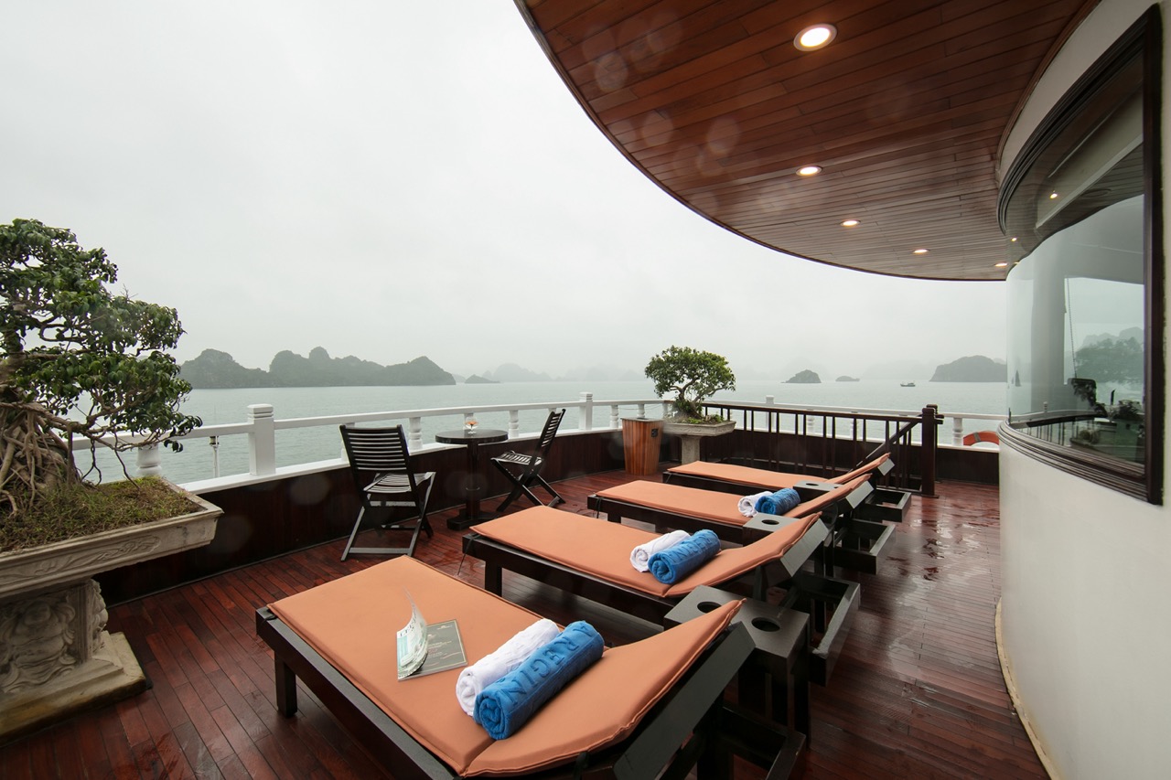 Scenic view of Halong Bay from a luxury cruise balcony with lounge chairs and relaxing atmosphere.