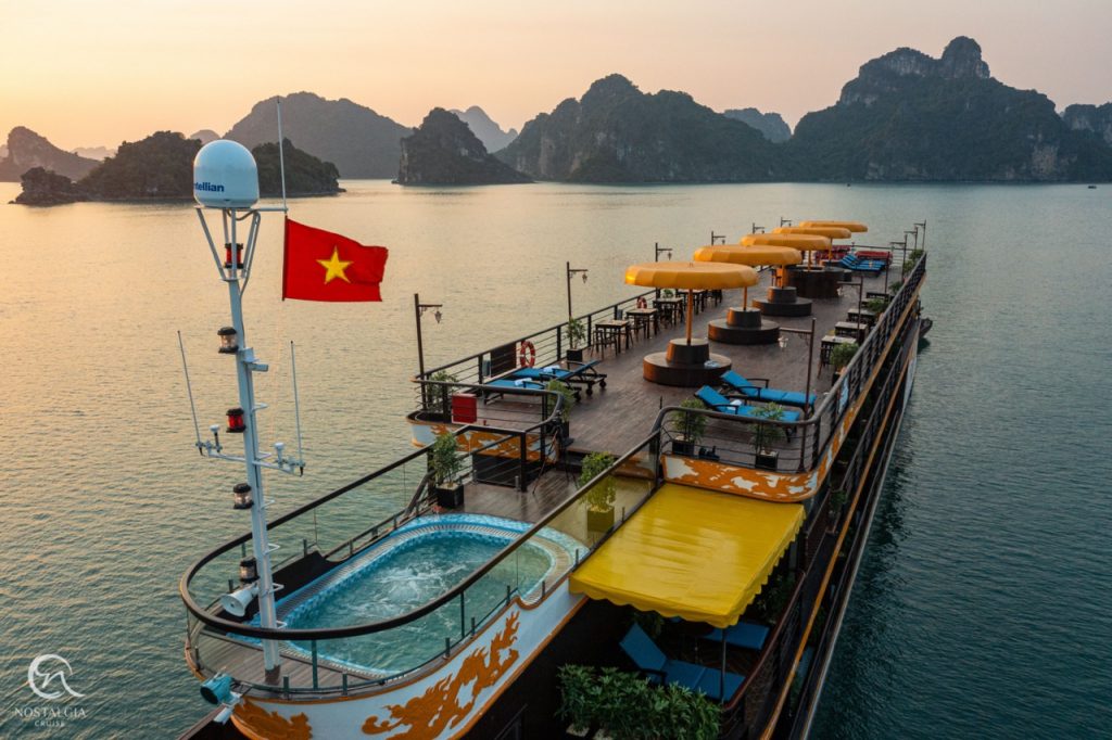 Scenic view of a luxury cruise boat with sun loungers and a hot tub on Halong Bay at sunset.