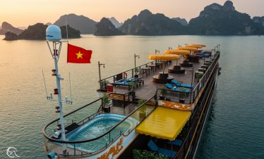 Scenic view of a luxury cruise boat with sun loungers and a hot tub on Halong Bay at sunset.