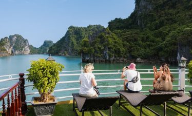Stunning view of Halong Bay with tourists relaxing on a cruise balcony, surrounded by lush green isl.