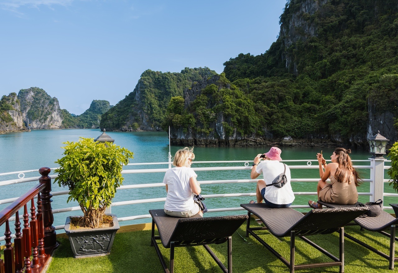 Stunning view of Halong Bay with tourists relaxing on a cruise balcony, surrounded by lush green isl.