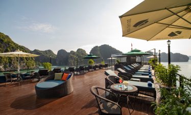Scenic view of a cruise balcony in Halong Bay with lounge chairs and umbrellas, overlooking limeston.