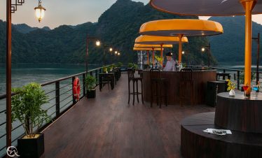 Relaxing cruise deck overlooking Halong Bay with scenic mountain views and cozy seating.