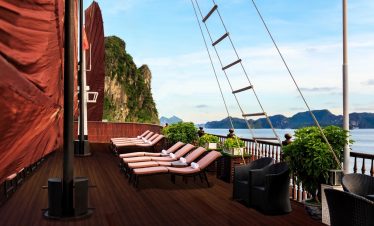 Stunning view of Halong Bay from a cruise balcony with lounge chairs and lush greenery.