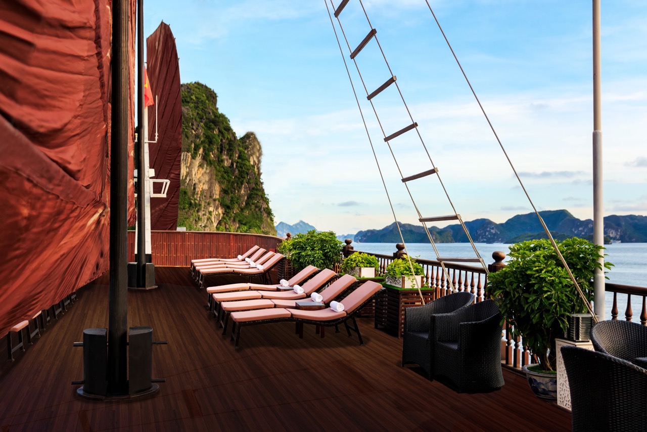Stunning view of Halong Bay from a cruise balcony with lounge chairs and lush greenery.