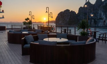 Sunset cruise balcony scene at Bai Tu Long Bay with scenic limestone karsts and calm waters.