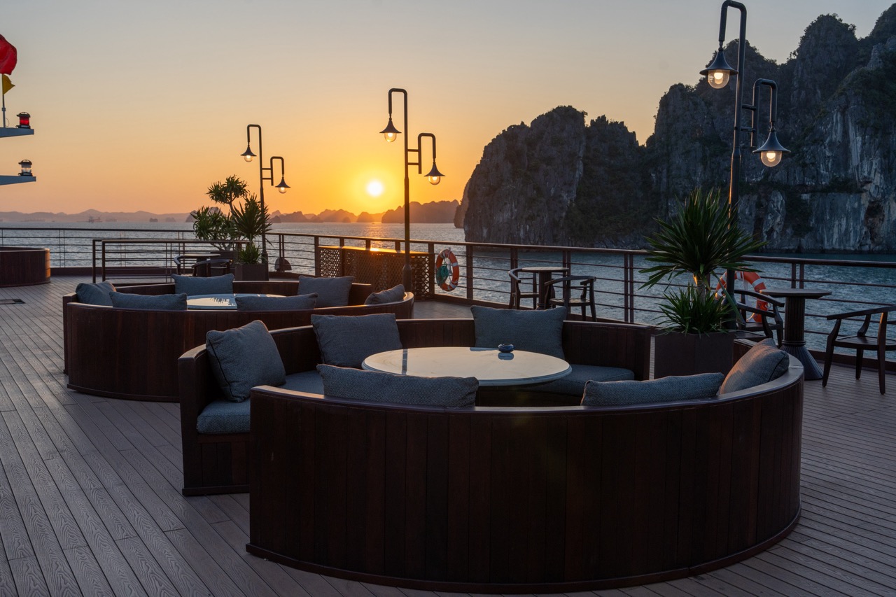 Sunset cruise balcony scene at Bai Tu Long Bay with scenic limestone karsts and calm waters.