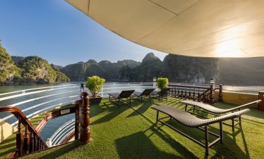 Stunning Halong Bay scenery from a cruise balcony with lounge chairs and lush greenery.