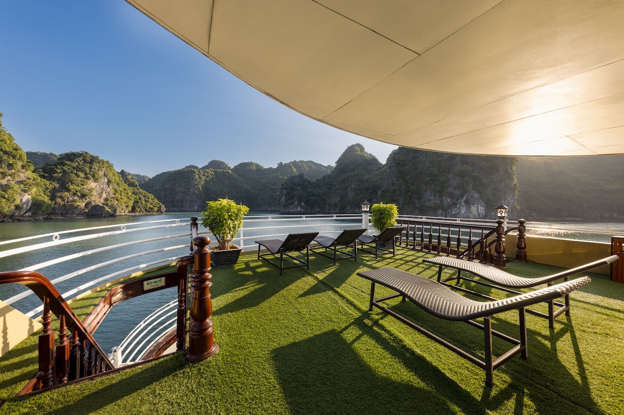 Stunning Halong Bay scenery from a cruise balcony with lounge chairs and lush greenery.
