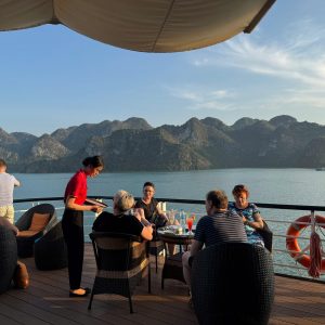 Relaxing cruise on Halong Bay with panoramic views of limestone karsts and a group enjoying dinner.