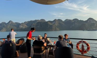 Relaxing cruise on Halong Bay with panoramic views of limestone karsts and a group enjoying dinner.