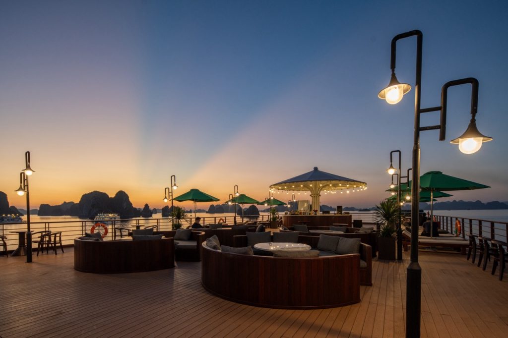 Sunset view from a Halong Bay cruise balcony with cozy seating and ambient lighting.