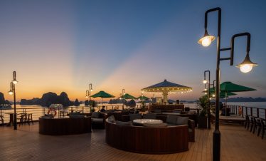 Sunset view from a Halong Bay cruise balcony with cozy seating and ambient lighting.