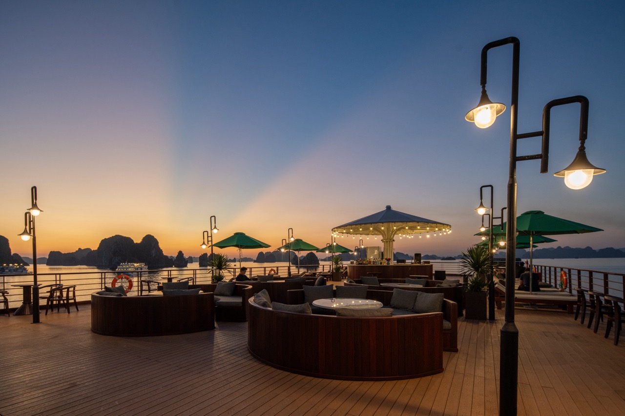 Sunset view from a Halong Bay cruise balcony with cozy seating and ambient lighting.