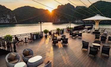 Stunning sunset view from a Halong Bay cruise balcony with seating area and scenic limestone islands.