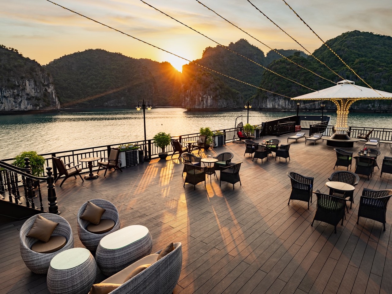 Stunning sunset view from a Halong Bay cruise balcony with seating area and scenic limestone islands.
