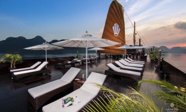 Luxurious cruise deck in Halong Bay with sun loungers, umbrellas, and scenic mountain views, perfect.