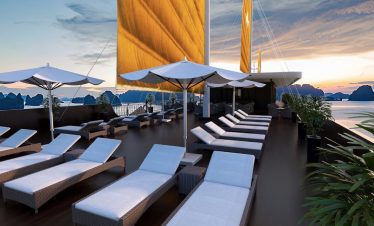 Luxury cruise balcony view of Lan Ha Bay at sunset with sun loungers and umbrellas.
