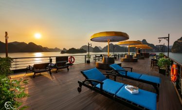 Halong Bay cruise balcony with sunset, lounge chairs, and scenic mountain views.