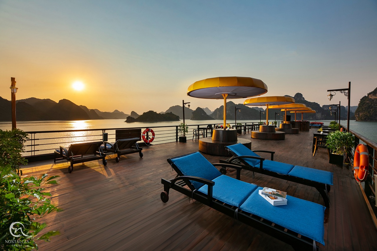 Halong Bay cruise balcony with sunset, lounge chairs, and scenic mountain views.