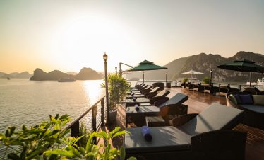 Stunning sunset view from a luxury cruise balcony in Halong Bay, with lounge chairs and scenic limes.