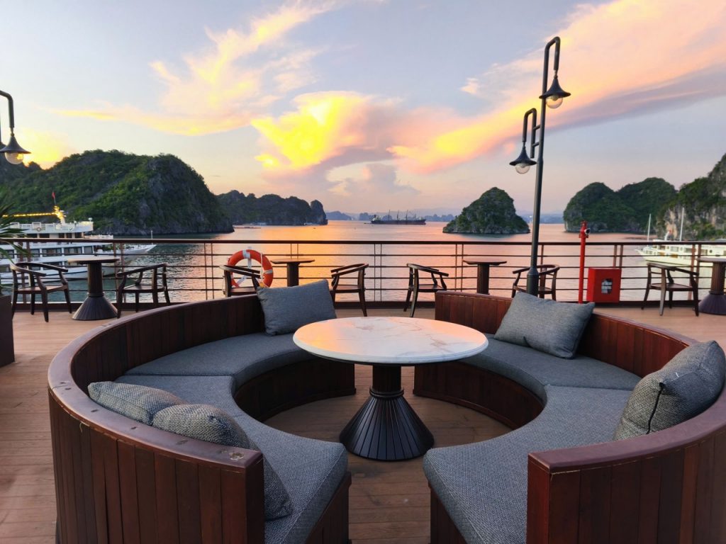 Scenic cruise balcony view of Bai Tu Long Bay at sunset with calm waters and lush islands.