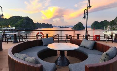 Scenic cruise balcony view of Bai Tu Long Bay at sunset with calm waters and lush islands.