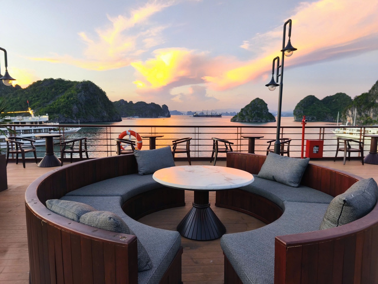 Scenic cruise balcony view of Bai Tu Long Bay at sunset with calm waters and lush islands.