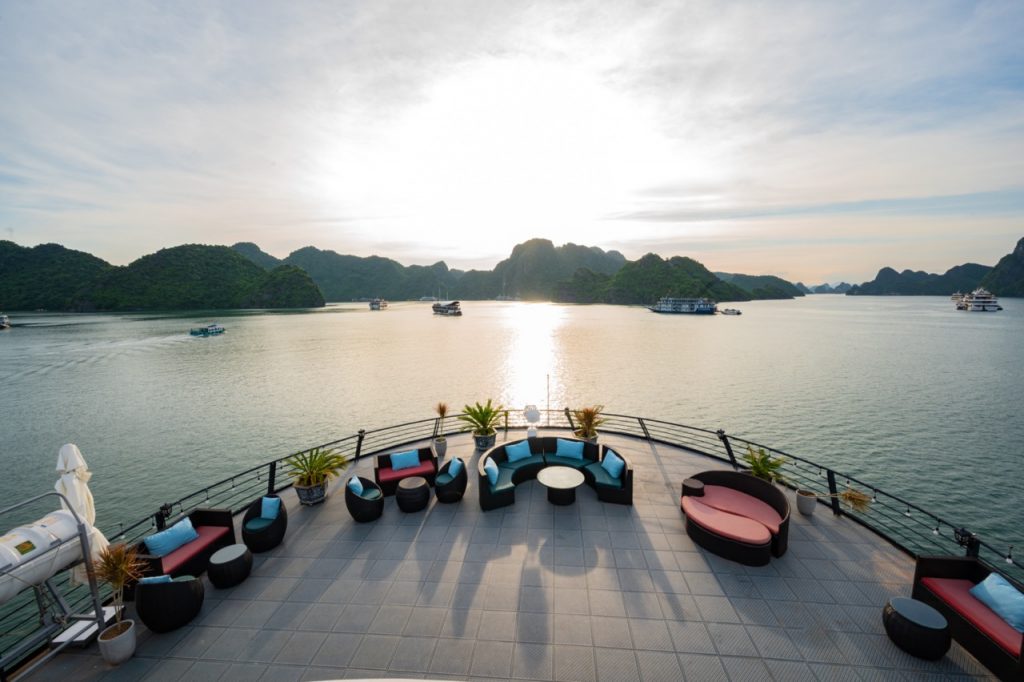 Sunset over Halong Bay with luxurious cruise balcony, scenic limestone islands, and tranquil waters.