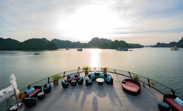 Sunset over Halong Bay with luxurious cruise balcony, scenic limestone islands, and tranquil waters.