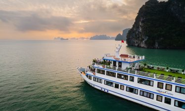Beautiful cruise ship sailing in Halong Bay at sunset, surrounded by limestone karsts and tranquil w.