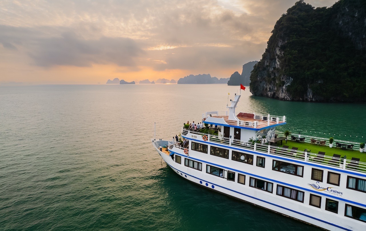 Beautiful cruise ship sailing in Halong Bay at sunset, surrounded by limestone karsts and tranquil w.