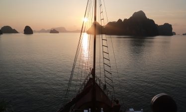 Sunset view from a Halong Bay cruise with limestone karsts and calm waters.