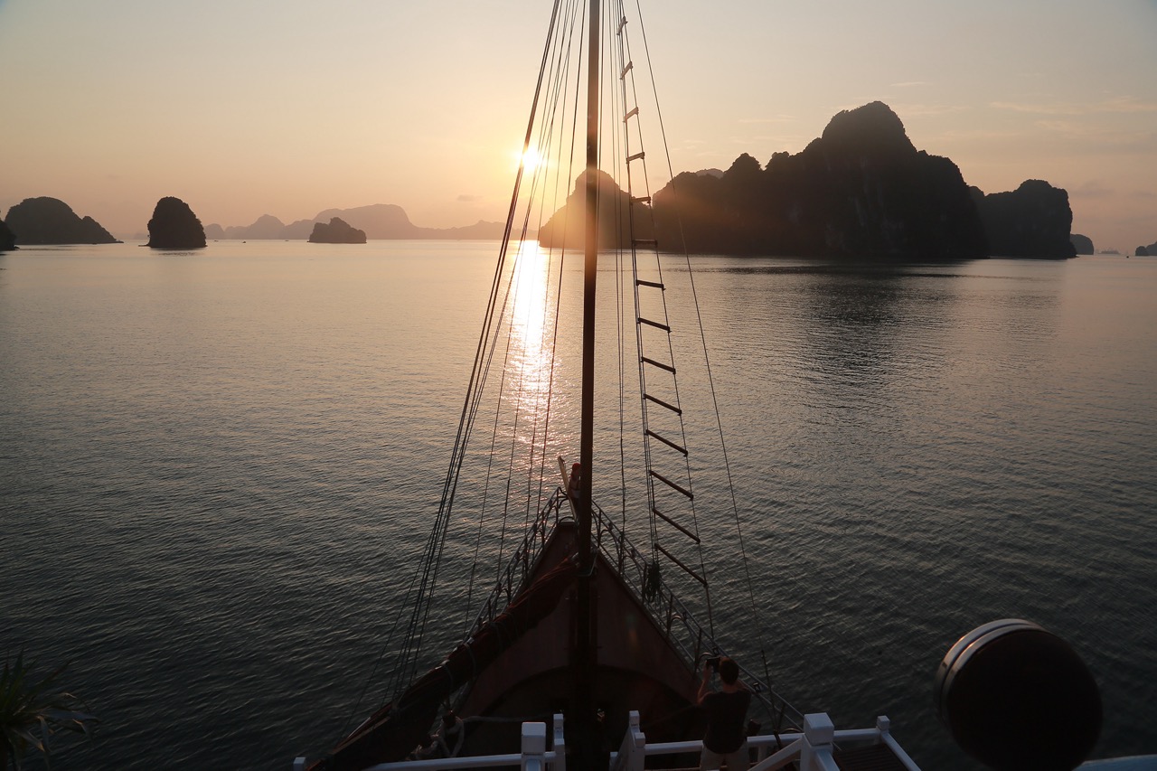 Sunset view from a Halong Bay cruise with limestone karsts and calm waters.