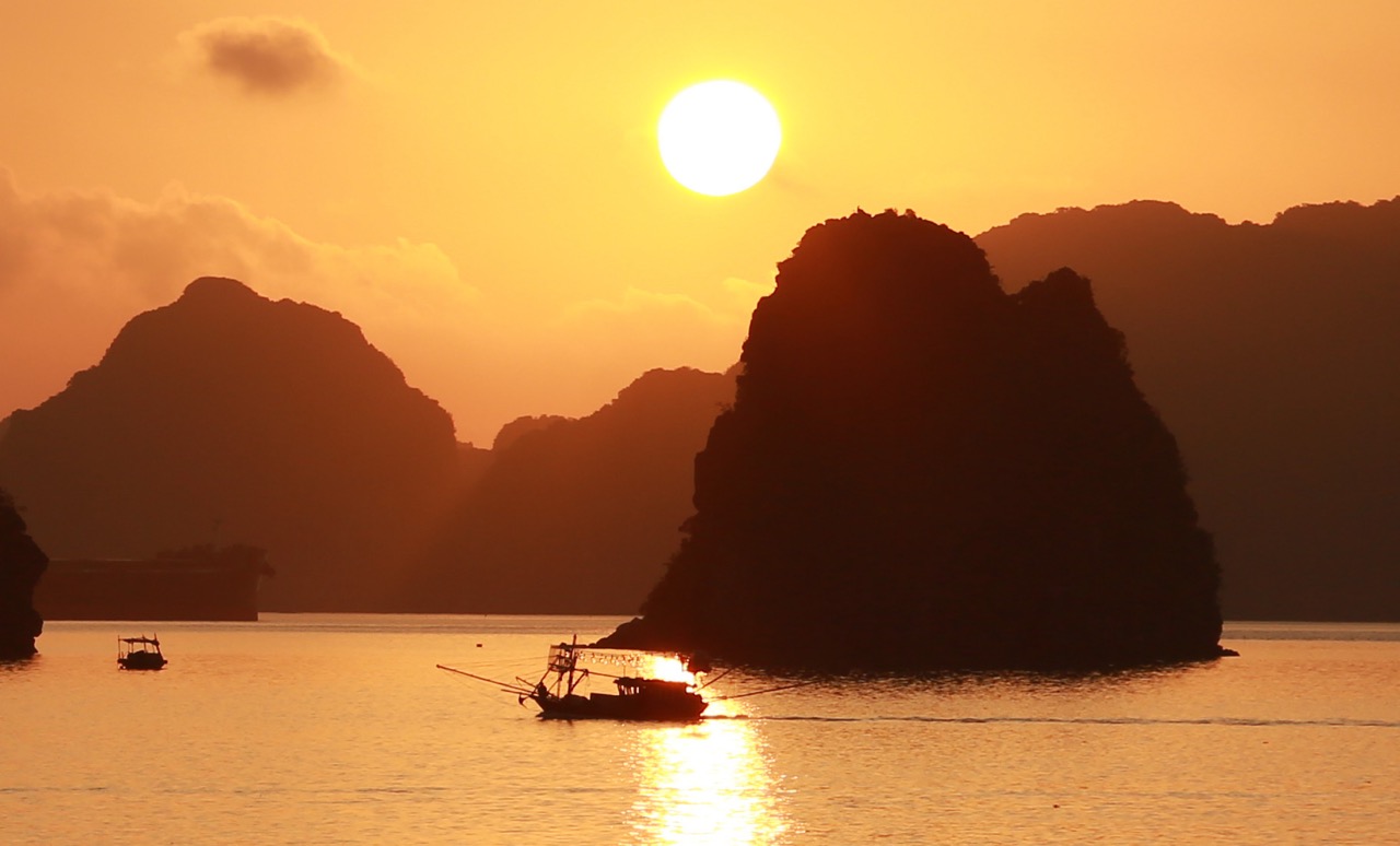 Sunset scene of Halong Bay with limestone islands, boats, and calm waters, perfect for cruise and si.