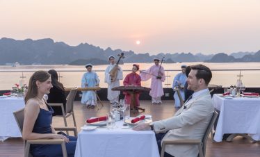 Romantic couple dining on a luxury cruise balcony in Halong Bay at sunset.
