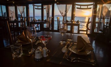 Elegant dining setup on Halong Bay cruise with sunset view and scenic ocean backdrop.