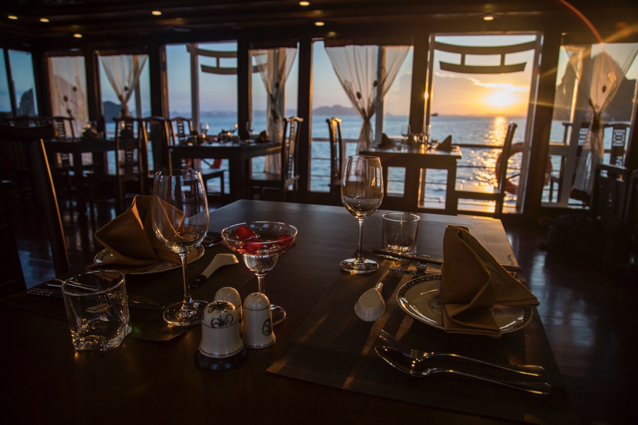 Elegant dining setup on Halong Bay cruise with sunset view and scenic ocean backdrop.