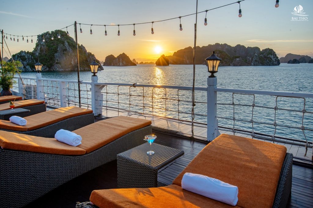 Sunset over Bai Tu Long Bay from cruise deck with lounge chairs and string lights, perfect for relax.
