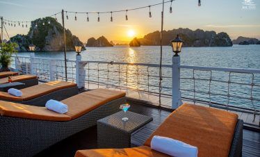 Sunset over Bai Tu Long Bay from cruise deck with lounge chairs and string lights, perfect for relax.