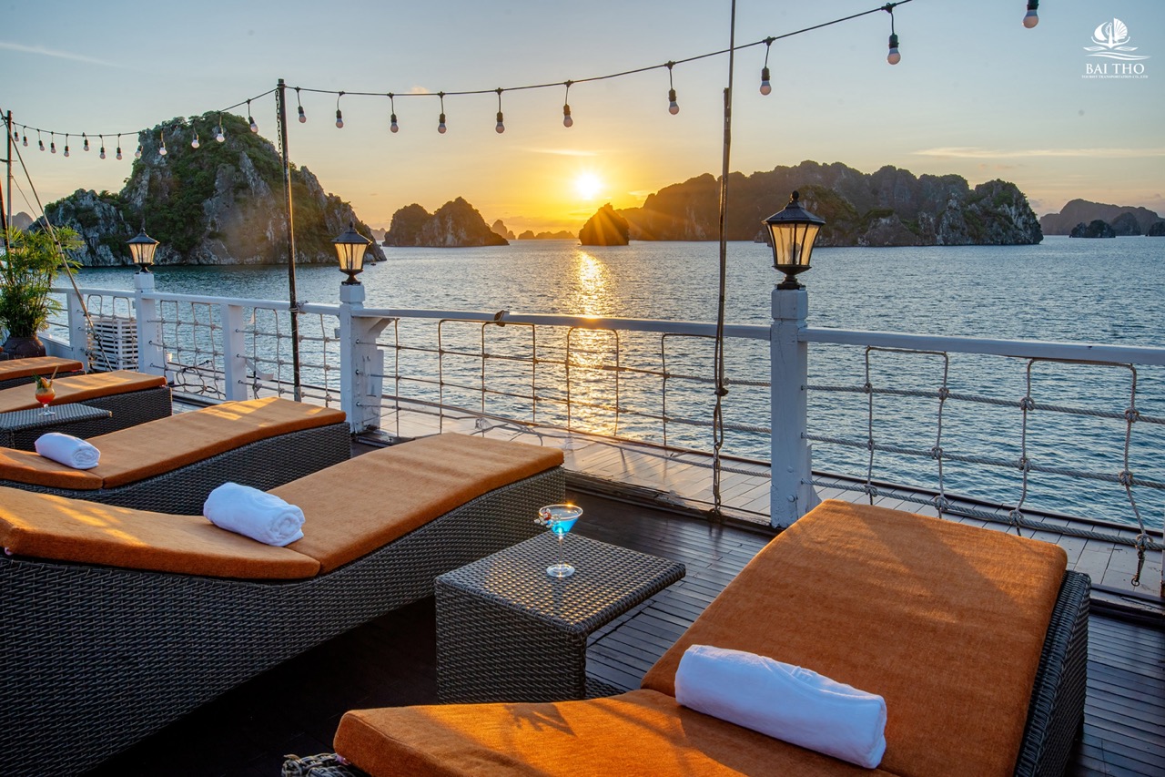 Sunset over Bai Tu Long Bay from cruise deck with lounge chairs and string lights, perfect for relax.