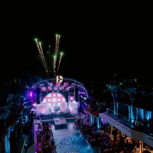 Nighttime music festival at a tropical resort with fireworks, colorful lights, and outdoor seating.