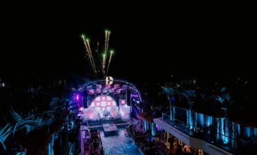 Nighttime music festival at a tropical resort with fireworks, colorful lights, and outdoor seating.