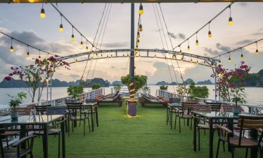 Stunning sunset view from cruise balcony in Halong Bay with seating area and vibrant flowers.