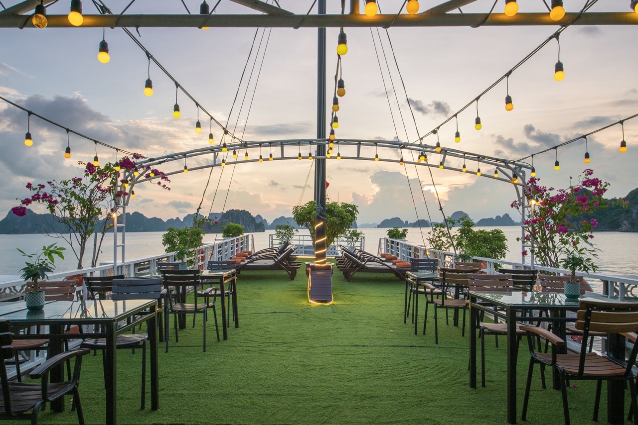 Stunning sunset view from cruise balcony in Halong Bay with seating area and vibrant flowers.
