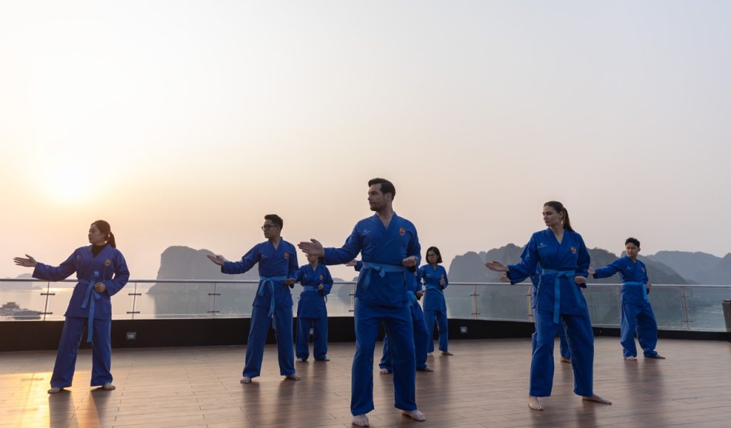 Calista Cruise Halong Bay Tai Chi session on deck with scenic limestone karsts in the background.