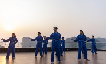 Calista Cruise Halong Bay Tai Chi session on deck with scenic limestone karsts in the background.