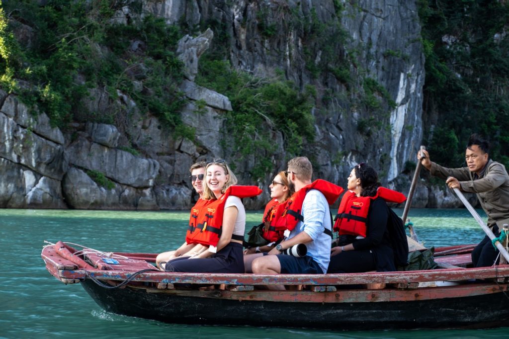 People kayaking on Bai Tu Long Bay with scenic limestone cliffs and lush greenery.