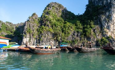Scenic view of boats anchored near towering limestone cliffs in Bai Tu Long Bay during daytime.